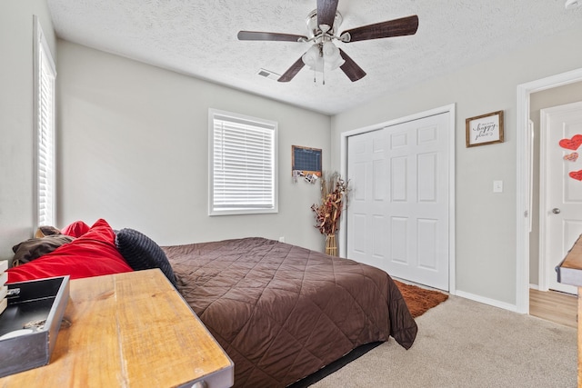 bedroom with a closet, baseboards, carpet flooring, a textured ceiling, and visible vents