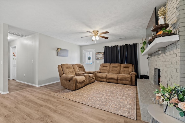 living area featuring visible vents, baseboards, a brick fireplace, ceiling fan, and wood finished floors