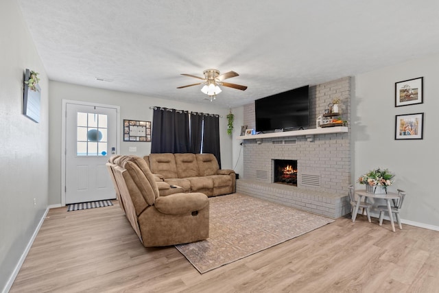 living area with light wood-style flooring, a ceiling fan, baseboards, and a fireplace