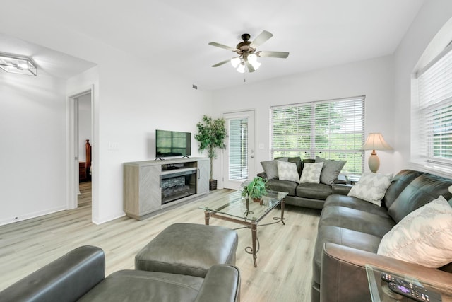 living area featuring light wood finished floors, ceiling fan, baseboards, and a fireplace