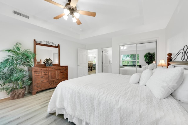 bedroom with visible vents, a closet, a raised ceiling, ceiling fan, and light wood finished floors