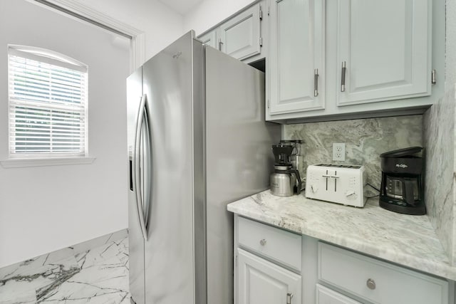 kitchen featuring tasteful backsplash, marble finish floor, light stone counters, and stainless steel fridge