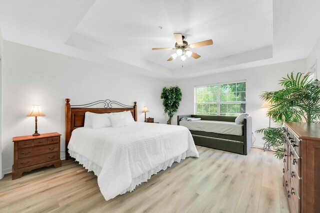 bedroom featuring ceiling fan, a raised ceiling, and light wood finished floors