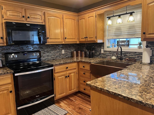 kitchen with dark stone countertops, a sink, black appliances, wood finished floors, and backsplash