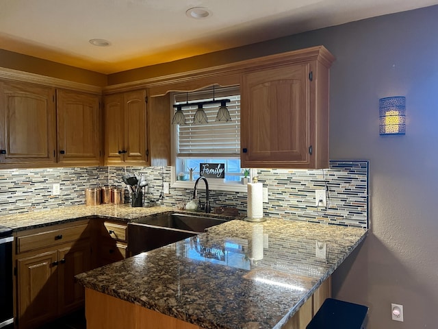 kitchen featuring dark stone countertops, a sink, a peninsula, brown cabinetry, and decorative backsplash