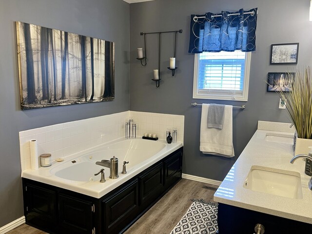bathroom featuring baseboards, a bath, a sink, double vanity, and wood finished floors