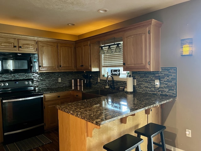 kitchen with a peninsula, backsplash, black appliances, dark stone counters, and a sink