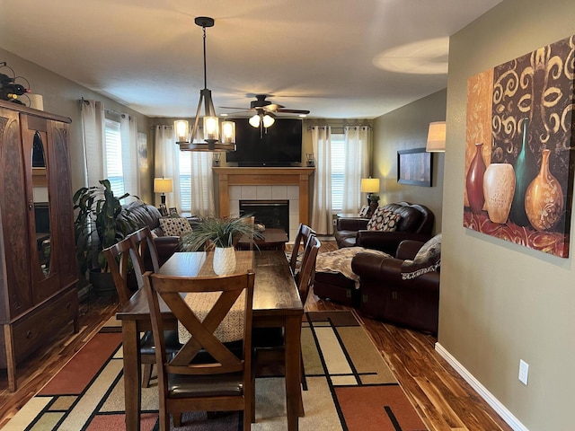 dining space featuring a tiled fireplace, baseboards, wood finished floors, and ceiling fan