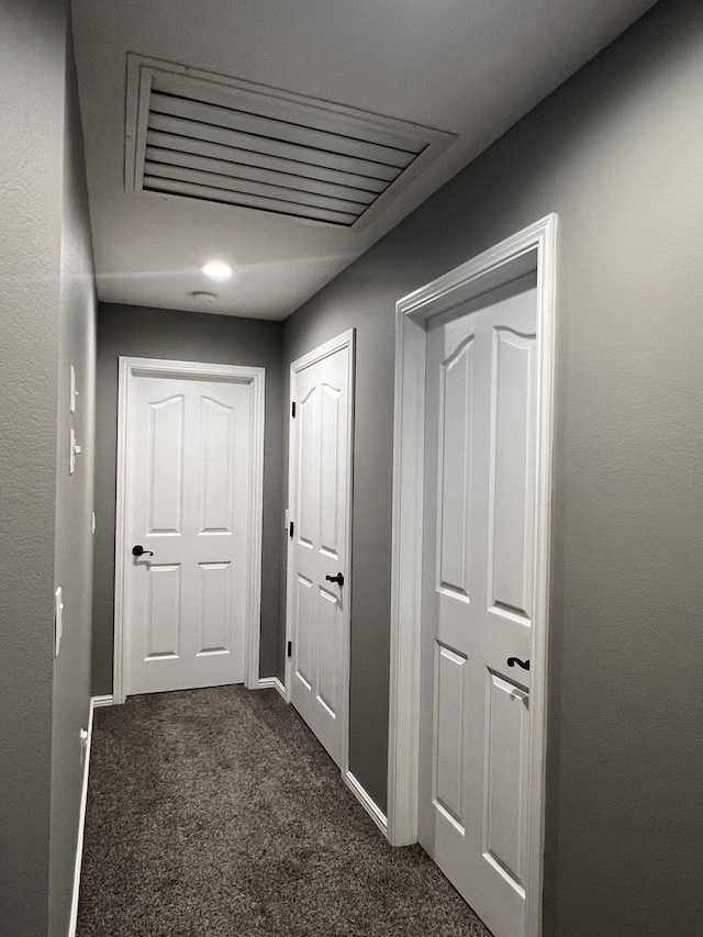 corridor featuring visible vents, baseboards, and dark carpet