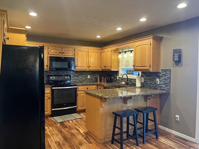 kitchen with a peninsula, black appliances, dark wood-type flooring, decorative backsplash, and a sink