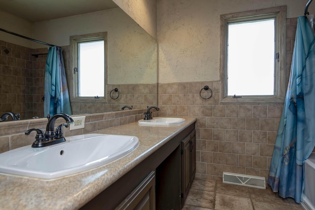 full bathroom featuring a sink, visible vents, tile walls, and double vanity