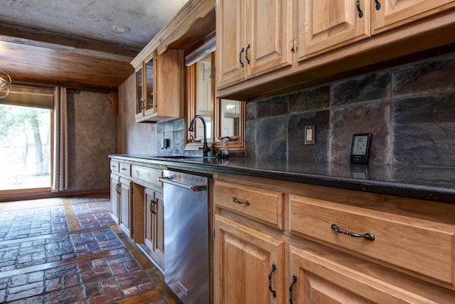 kitchen featuring dark countertops, decorative backsplash, stainless steel dishwasher, brick floor, and a sink