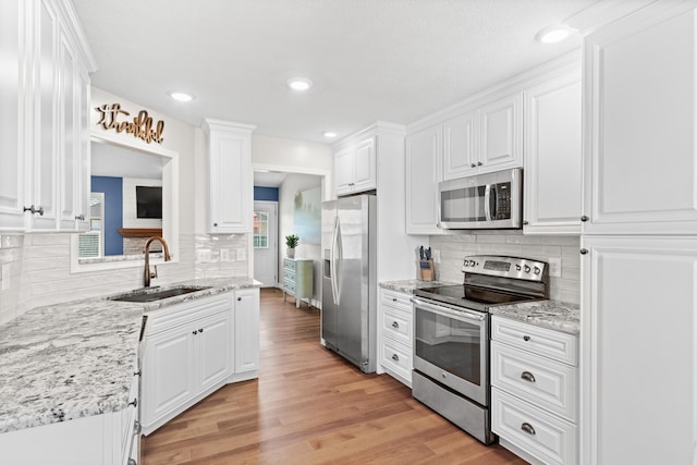 704 E Waterford Blvd, Ozark, MO 65721 - kitchen featuring light wood-style floors, white cabinetry, a sink, stainless steel appliances, and decorative backsplash