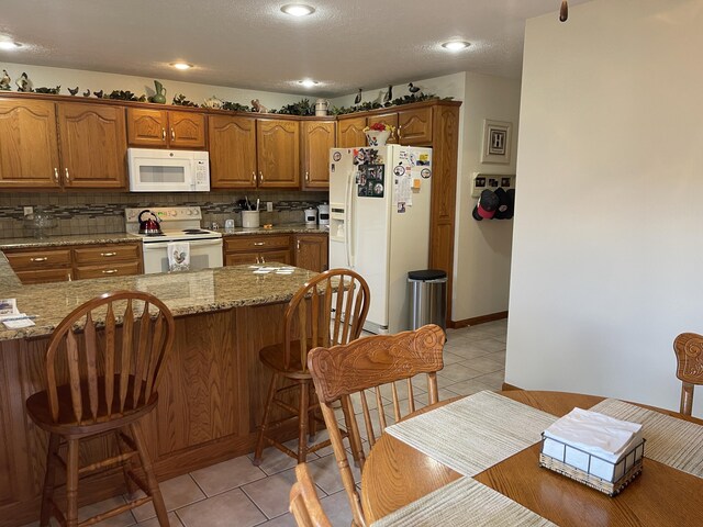 1605 S Meadow Ln, Bolivar, MO 65613 - kitchen featuring brown cabinetry, light tile patterned flooring, white appliances, and a kitchen breakfast bar