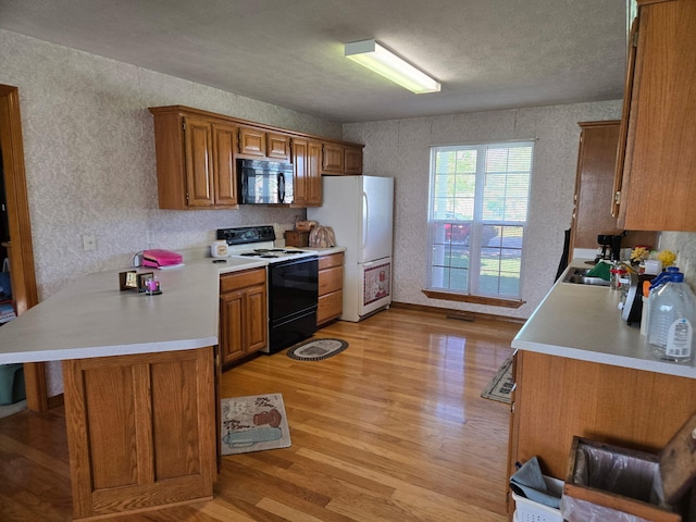 kitchen with light countertops, light wood-type flooring, electric stove, brown cabinetry, and black microwave