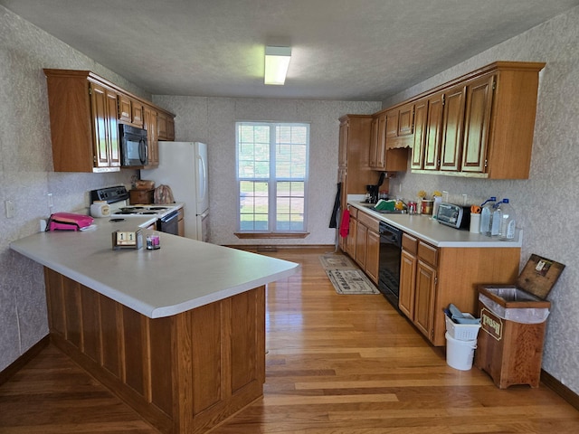 kitchen featuring light wood-style flooring, a peninsula, black appliances, light countertops, and brown cabinets