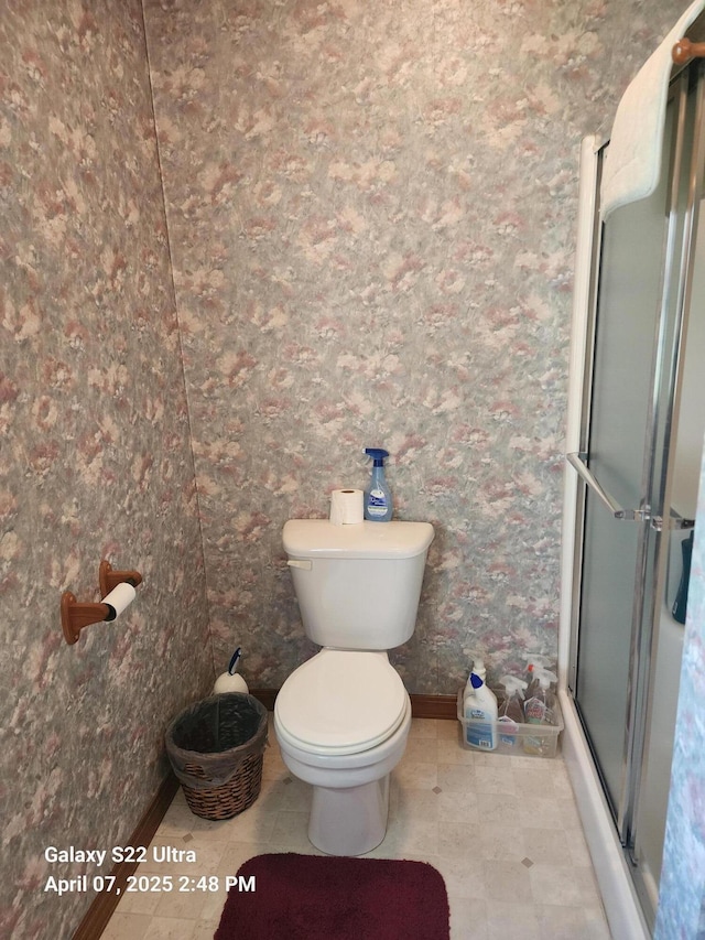 bathroom featuring toilet, baseboards, and a shower stall
