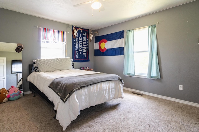 bedroom featuring ceiling fan, visible vents, multiple windows, and carpet floors