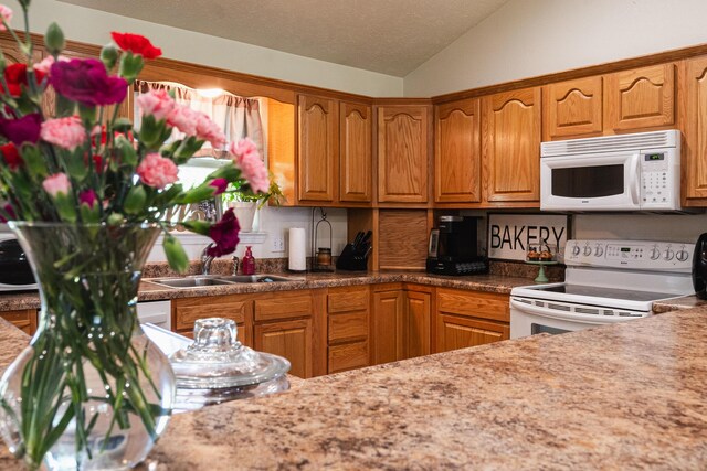 kitchen featuring brown cabinetry, a sink, white appliances, and lofted ceiling