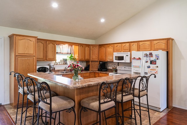 kitchen with white appliances, a breakfast bar, a sink, brown cabinets, and light wood finished floors