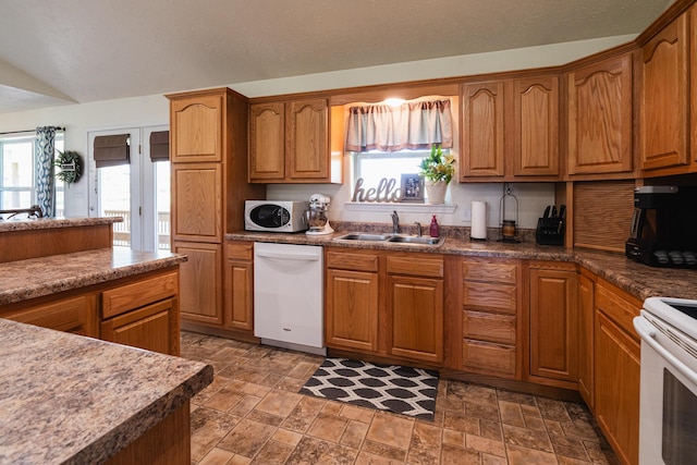 kitchen featuring brown cabinetry, a sink, white appliances, and stone finish flooring