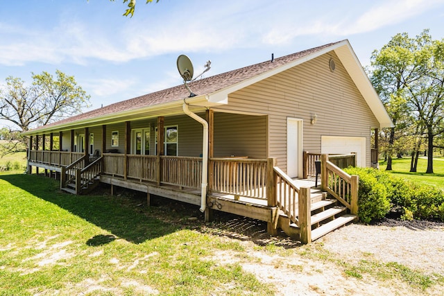 rear view of property featuring a yard, an attached garage, and a shingled roof