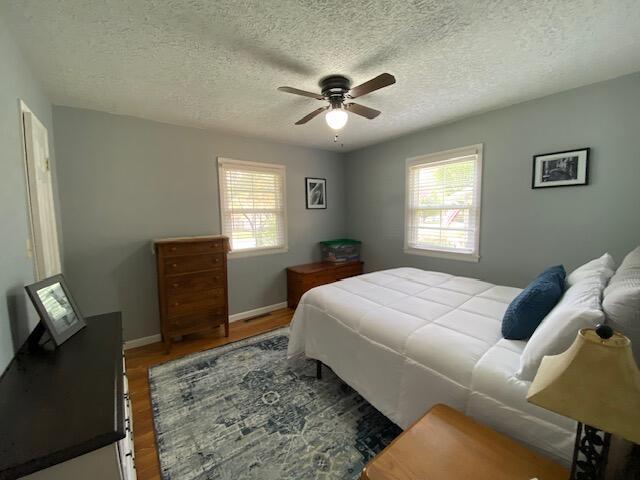 bedroom with baseboards, ceiling fan, wood finished floors, and a textured ceiling