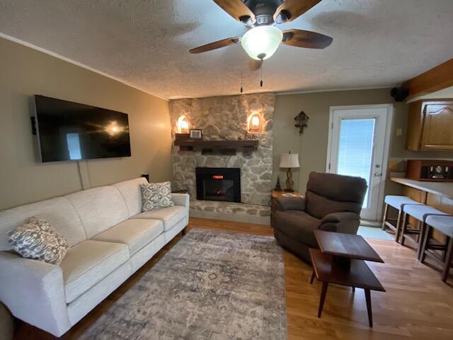 living room featuring a fireplace, ceiling fan, light wood-style floors, and a textured ceiling