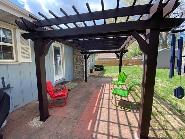 view of patio / terrace with a pergola, a shed, fence, and an outbuilding