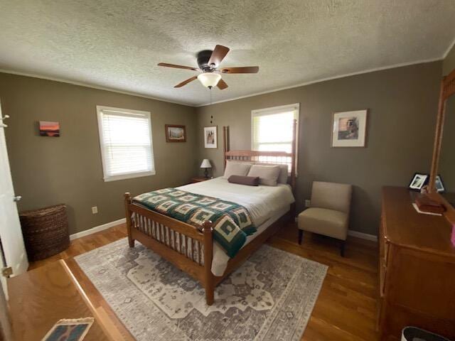 bedroom featuring a textured ceiling, wood finished floors, baseboards, and ornamental molding