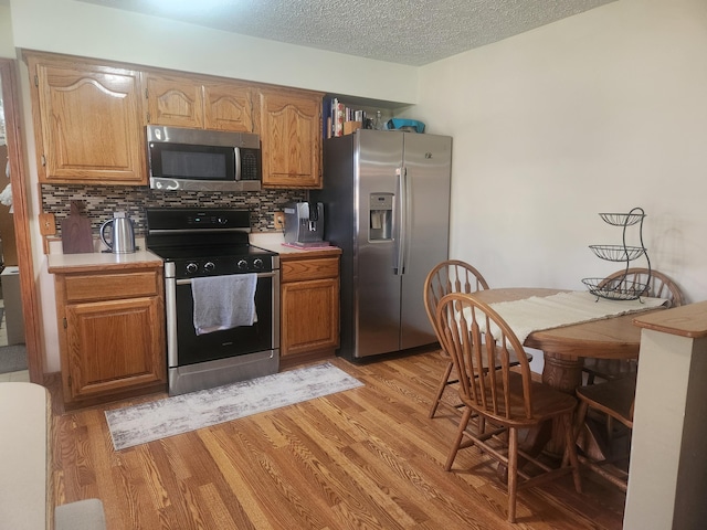 kitchen with tasteful backsplash, light countertops, a textured ceiling, light wood finished floors, and stainless steel appliances