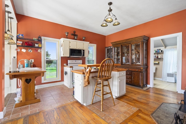 kitchen featuring white cabinets, hardwood / wood-style floors, stainless steel microwave, white range with electric stovetop, and plenty of natural light