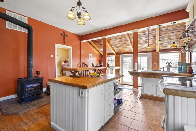 kitchen featuring visible vents, lofted ceiling with beams, a wood stove, white cabinetry, and wood counters