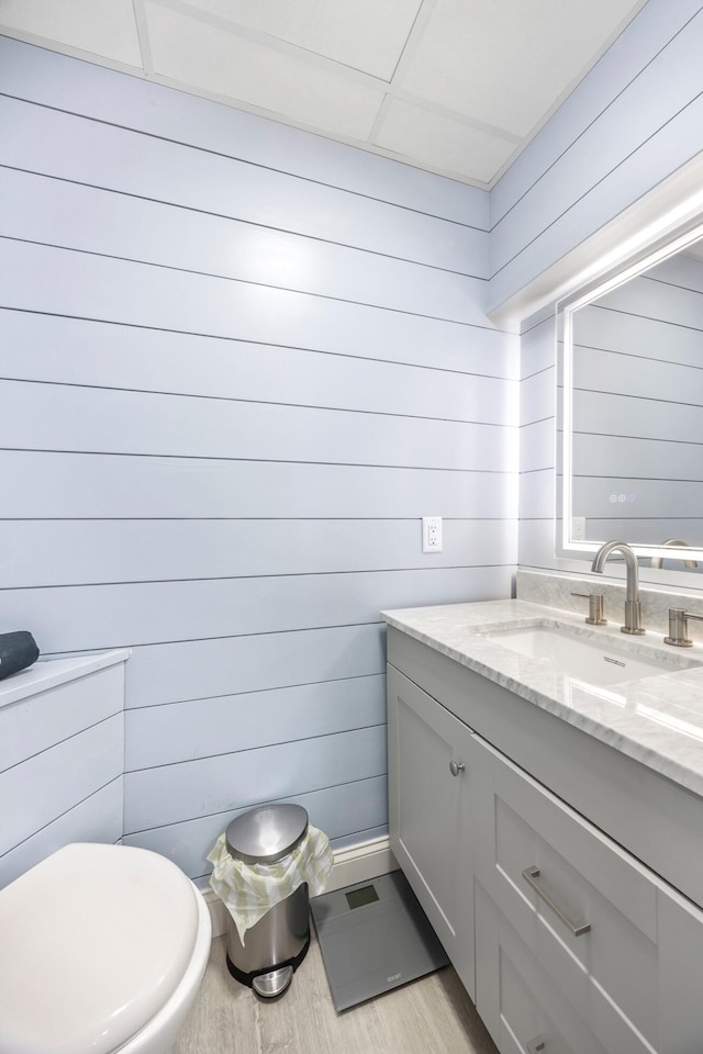 half bathroom featuring vanity, wood walls, toilet, and wood finished floors