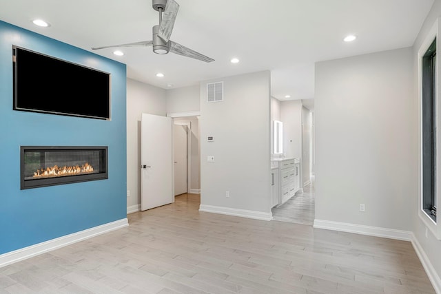 unfurnished living room with ceiling fan, light wood finished floors, a glass covered fireplace, recessed lighting, and baseboards
