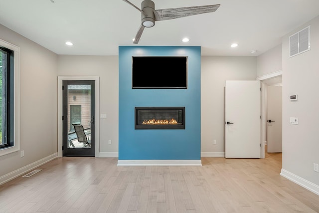 unfurnished living room featuring healthy amount of natural light, light wood-type flooring, a ceiling fan, a glass covered fireplace, and recessed lighting