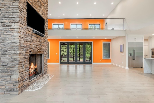 unfurnished living room featuring recessed lighting, a fireplace, baseboards, and a high ceiling