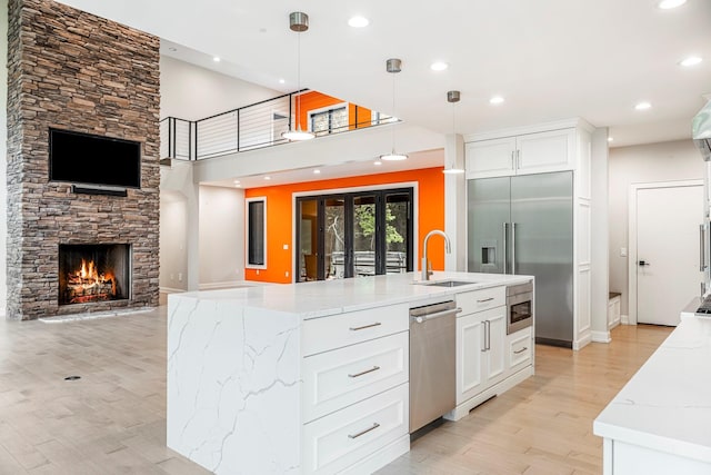 kitchen with built in appliances, a sink, light wood-style floors, recessed lighting, and light stone counters