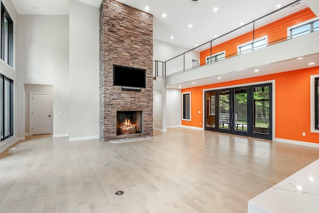 unfurnished living room featuring a towering ceiling, a stone fireplace, light wood-type flooring, baseboards, and recessed lighting