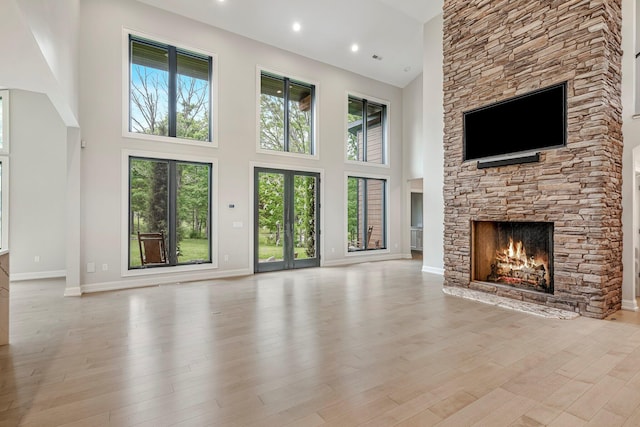 unfurnished living room featuring a fireplace, a high ceiling, baseboards, and light wood-type flooring
