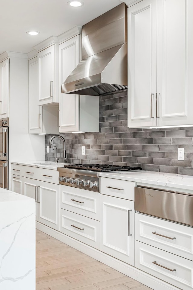 kitchen featuring wall chimney exhaust hood, a warming drawer, white cabinets, stainless steel gas cooktop, and recessed lighting