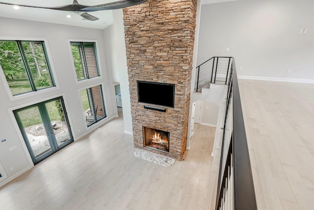 unfurnished living room with a stone fireplace, a ceiling fan, light wood-style floors, baseboards, and a high ceiling