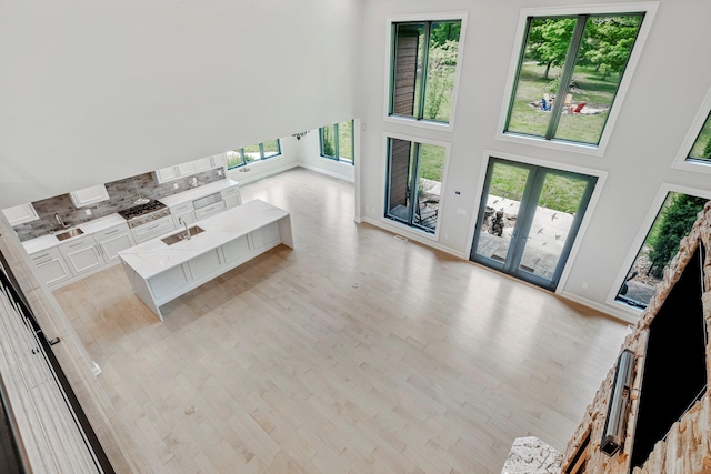 unfurnished living room with a high ceiling, light wood-style floors, baseboards, and a sink