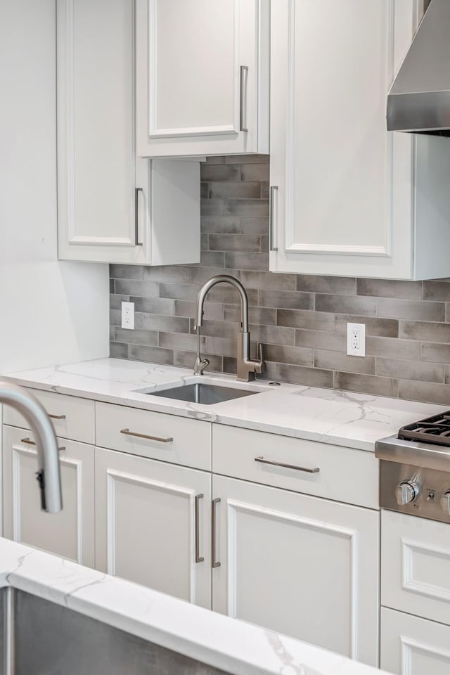 kitchen with wall chimney range hood, a sink, white cabinets, and decorative backsplash