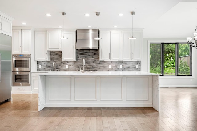 kitchen featuring wall chimney range hood, stainless steel appliances, tasteful backsplash, a sink, and recessed lighting
