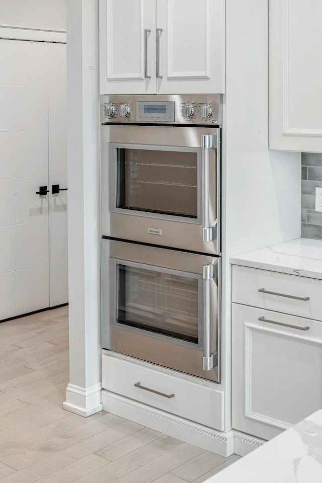 kitchen featuring double oven, white cabinetry, and light stone countertops