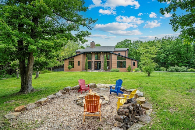 rear view of house with an outdoor fire pit, a chimney, and a yard