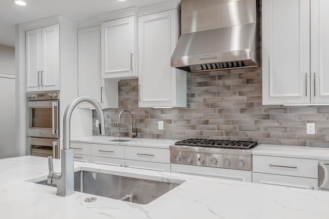 kitchen with wall chimney exhaust hood, white cabinetry, light stone countertops, and recessed lighting
