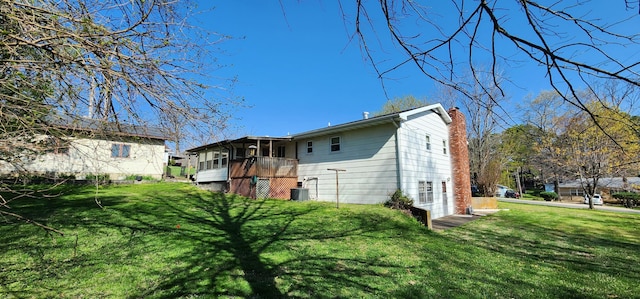 rear view of house with a sunroom, a yard, central AC, and a chimney