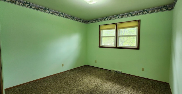 spare room with dark colored carpet, visible vents, and baseboards